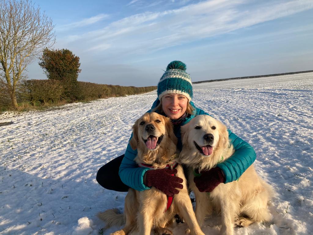 Gemma Cliffin MRCVS in the snow, hugging two golden retrievers