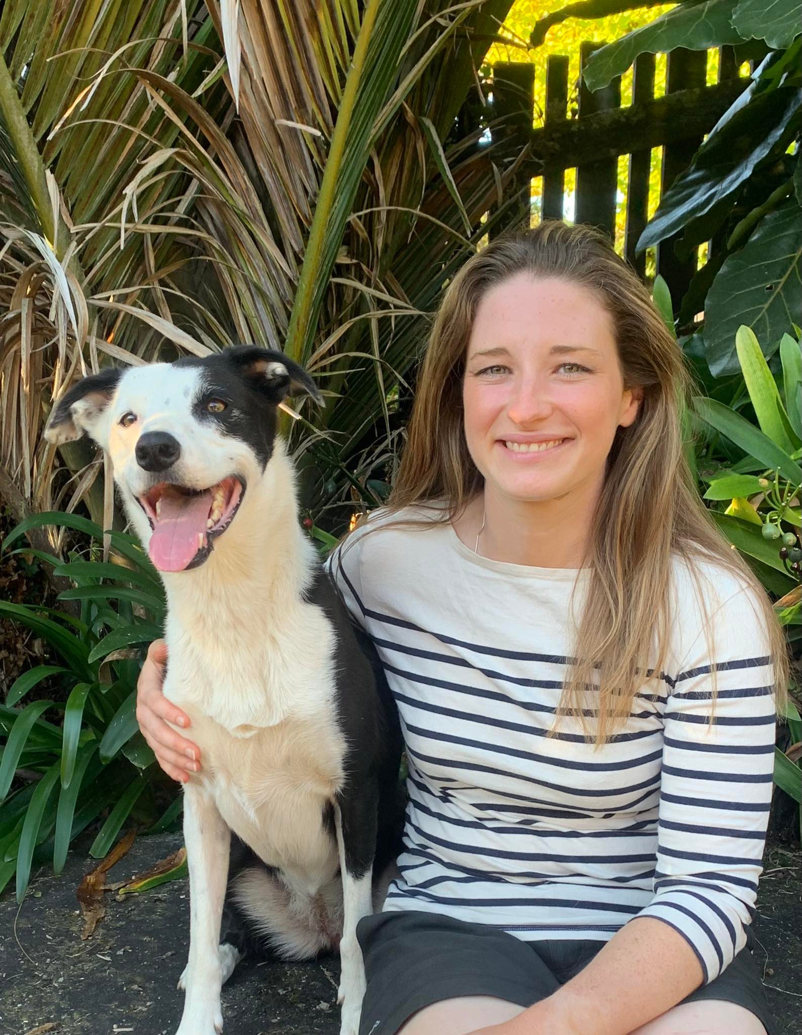 Alexandra Warner, pet content writer, with her dog Juno. (A white woman wearing a striped jumper is sitting on a rock with her arm round a black and white, medium sized dog.